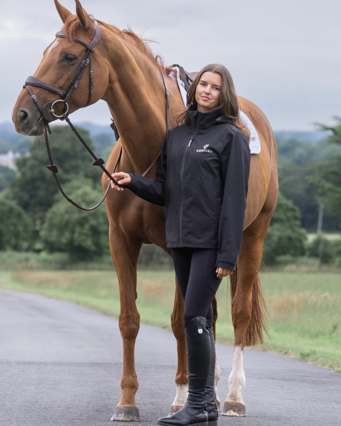 Black coloured Equidry Womens Nimbus Pack Away Jacket with Stowaway Hood on street background #colour_black