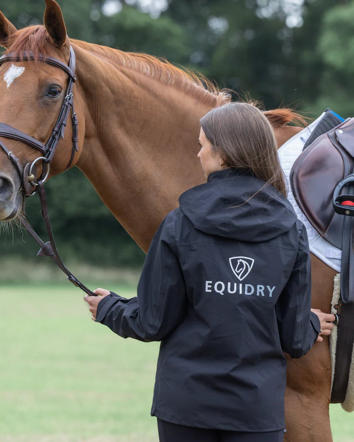 Black coloured Equidry Womens Nimbus Pack Away Jacket with Stowaway Hood on street background #colour_black