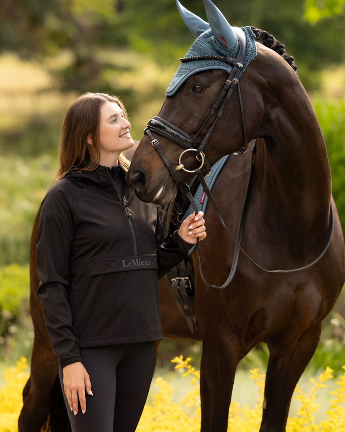 Black coloured LeMieux Womens Perri Half Zip Waterproof Jacket on tree background #colour_black