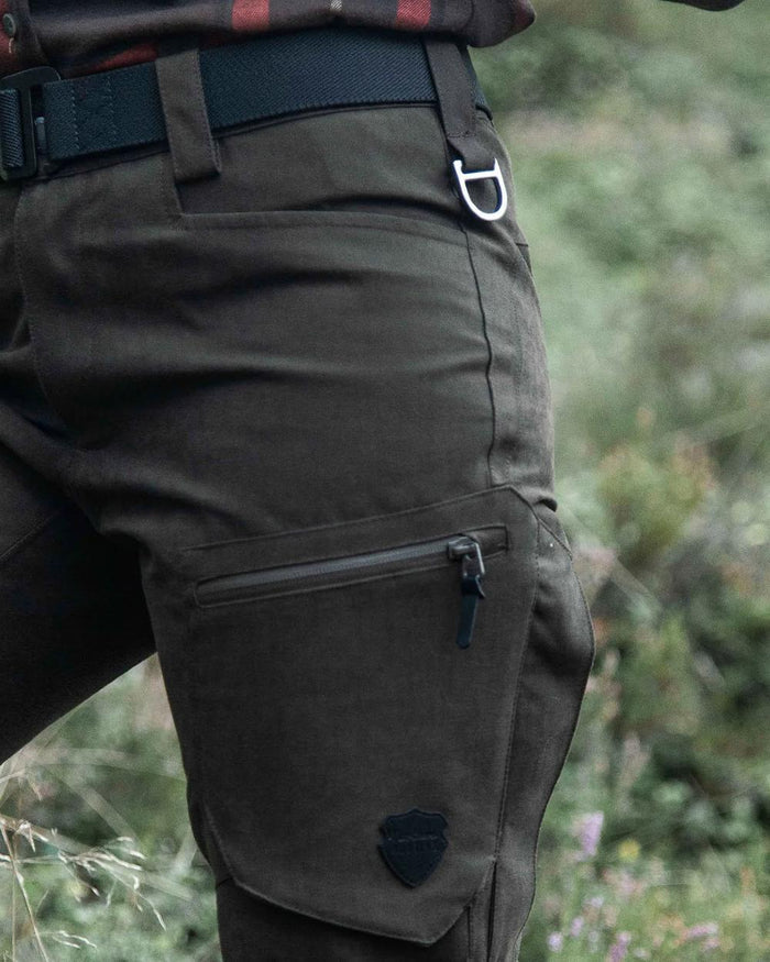 Dark Green coloured Northern Hunting Womens Alva Una G2 Hunting Trousers on forest background #colour_dark-green