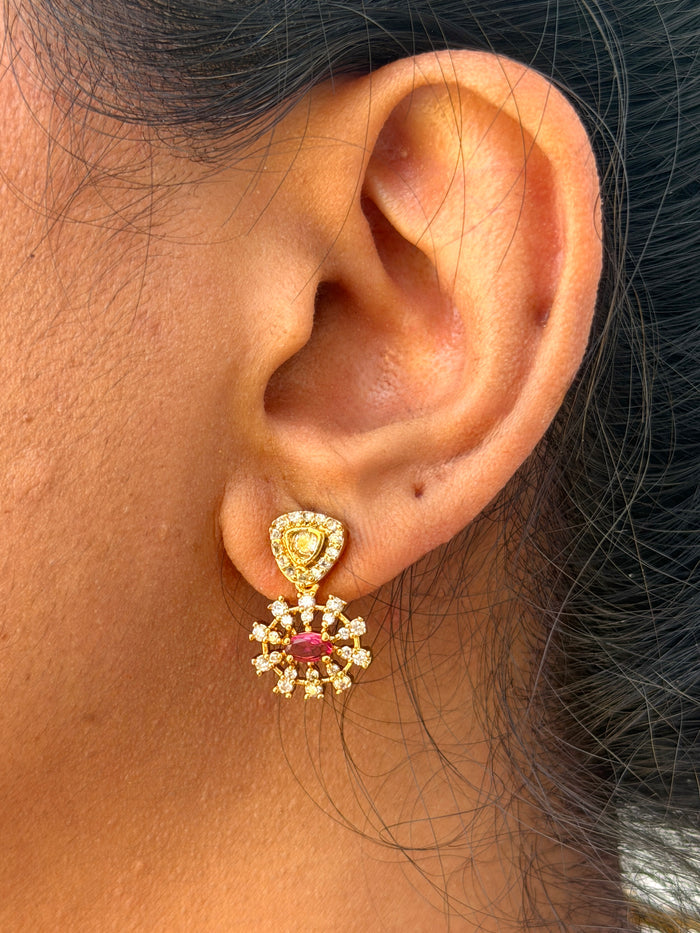 ear wearing a gold earring with a pink gemstone.