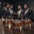Custom engraved whiskey glasses with bold etched initials filled with bourbon on a wooden bar, personalized monogram rocks glasses for men, sophisticated barware set perfect for groomsmen gifts, best man gift, Father’s Day or anniversary, modern custom scotch glasses for home bar or office.