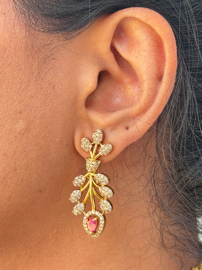 Close-up of an ear wearing a decorative gold earring with a pink gemstone.